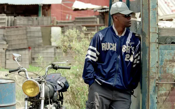 4K Ultra HD PC wallpaper: gritty Man on Fire (2004)–style gangster scene — a man in a navy jacket and cap leans by a doorway next to a motorcycle in a sunlit, rundown lot.