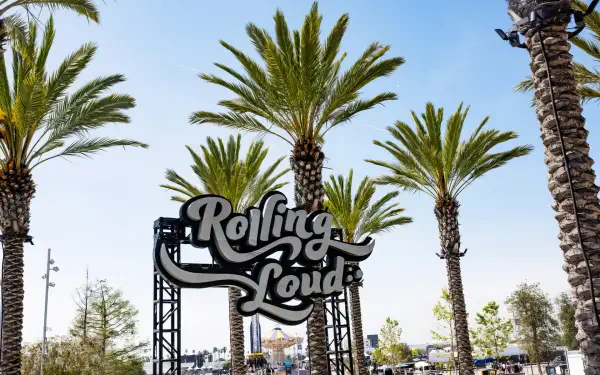 HD PC desktop wallpaper background: outdoor music festival scene with palm trees framing a Rolling Loud entrance sign beneath a clear blue sky.