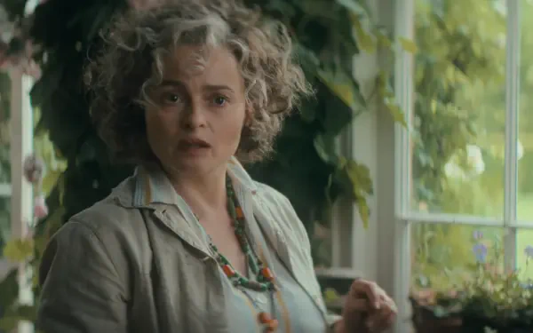 HD PC wallpaper: actress from TV series Agatha Christie's Seven Dials, curly-haired in a light blouse and beads, startled expression near a sunlit window framed by greenery.