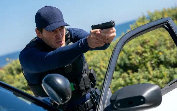 4K Ultra HD PC wallpaper: a uniformed police officer by a patrol car aiming a handgun, action scene from the movie Mercy (2026), featuring the film’s lead actor.