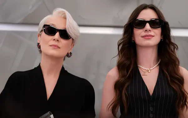 4K Ultra HD desktop wallpaper for The Devil Wears Prada 2: two stylish women in sunglasses and tailored black outfits, striking confident poses against a minimalist, neutral backdrop.