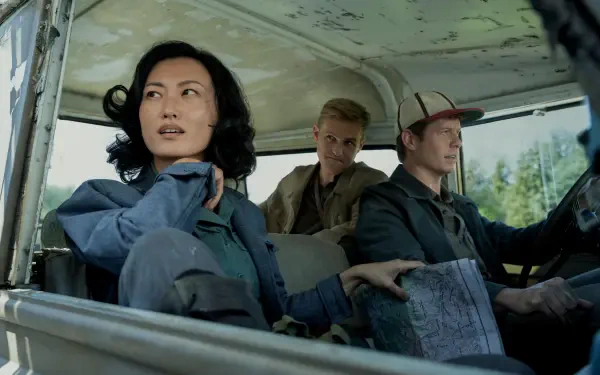 8K Ultra HD PC desktop wallpaper from the movie Monarch: Legacy of Monsters — three characters in a weathered jeep: a woman in the front passenger seat looking out, two men driving and consulting a map.