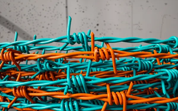 Close-up 4K Ultra HD PC desktop wallpaper of intertwined turquoise and orange barbed wire against a blurred concrete background.