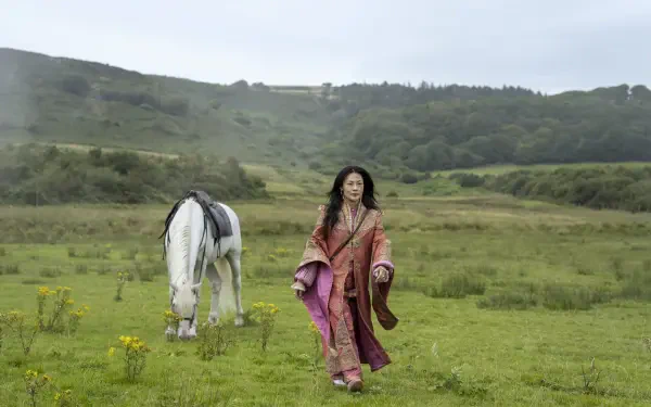 4K Ultra HD PC desktop wallpaper from the TV show Young Sherlock: a woman in a flowing pink robe walks across a green meadow beside a white horse with rolling hills under a pale sky.