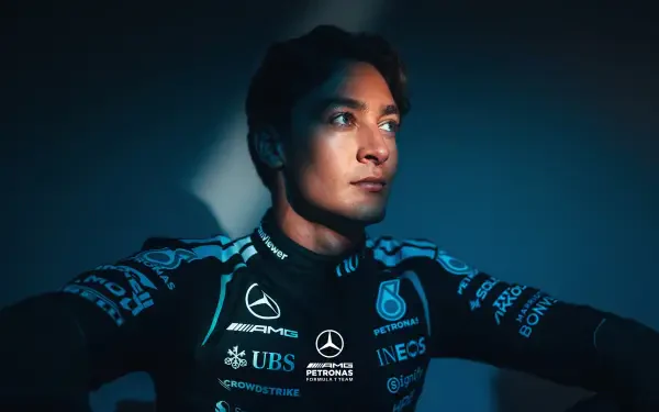 Moody portrait of a Mercedes AMG F1 driver in team race suit, gazing into light — 2K Quad HD PC desktop wallpaper/background with F1 racing theme.