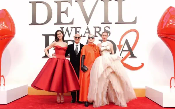 2K Quad HD desktop wallpaper: red-carpet portrait of The Devil Wears Prada 2 principal cast in elegant gowns and suits before a large logo and oversized red-heel props.