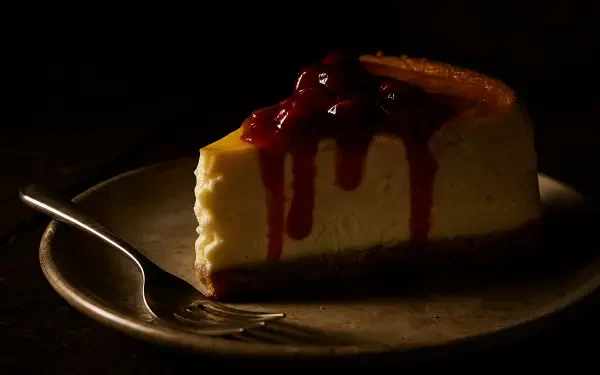 Cherry-topped cheesecake slice on a plate with a fork in low light, rich texture and deep shadows — 4K Ultra HD PC desktop wallpaper and background.