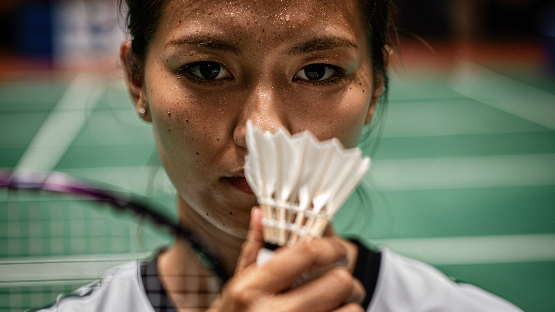 Close-up of a badminton player holding a shuttlecock to her face with racket and court blurred behind — 4K Ultra HD PC desktop wallpaper and background.