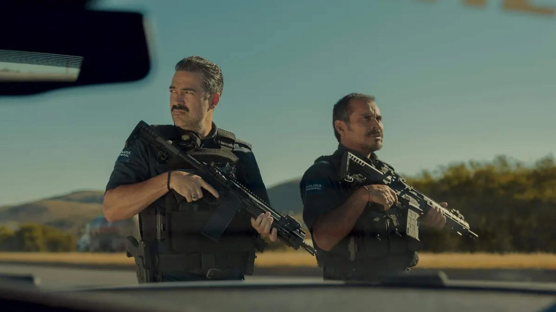 Two armed officers stand alert in a sunlit roadside standoff, cinematic tension — 4K Ultra HD PC desktop wallpaper background.