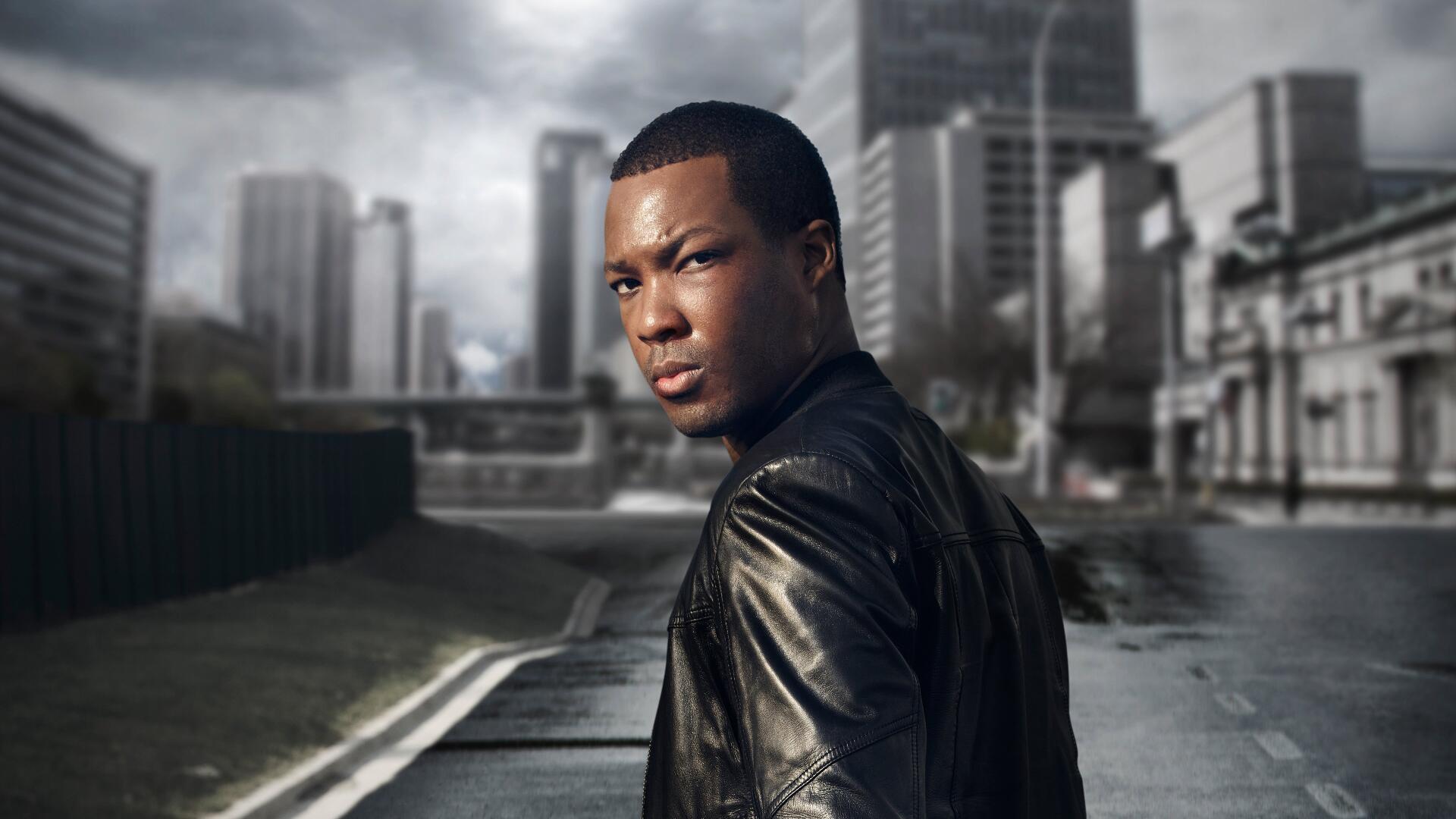 24: Legacy — 4K Ultra HD PC desktop wallpaper: a person in a leather jacket glances over their shoulder on a moody urban street with a towering skyline.