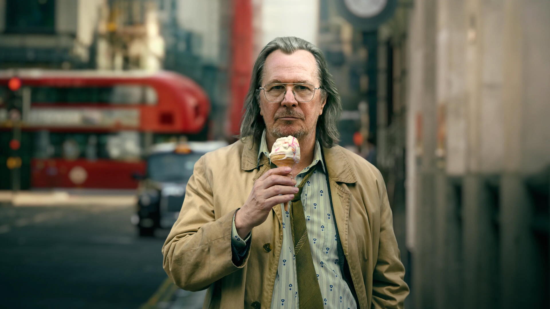 Slow Horses 4K Ultra HD PC desktop wallpaper and background: man in beige coat eating an ice cream on a London street with a blurred red double-decker bus behind him.