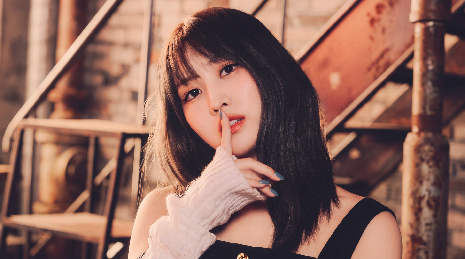 5K desktop wallpaper of a Japanese k-pop idol–style model posing finger-to-lips on an industrial staircase, warm soft lighting.