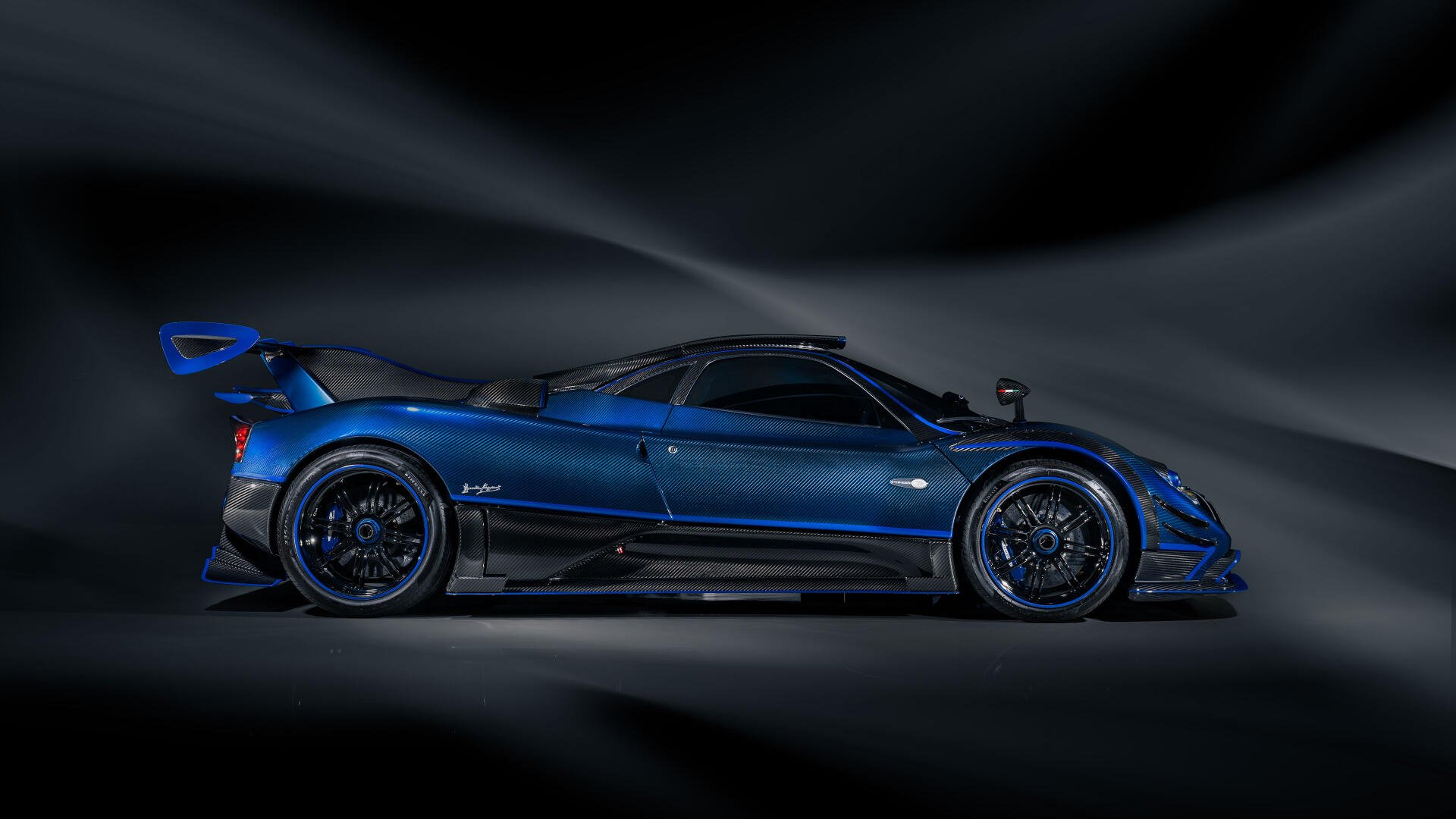 Side profile of a blue Pagani Zonda racing car with aerodynamic wings and carbon accents against a dark, streaked background — 4K Ultra HD PC desktop wallpaper.