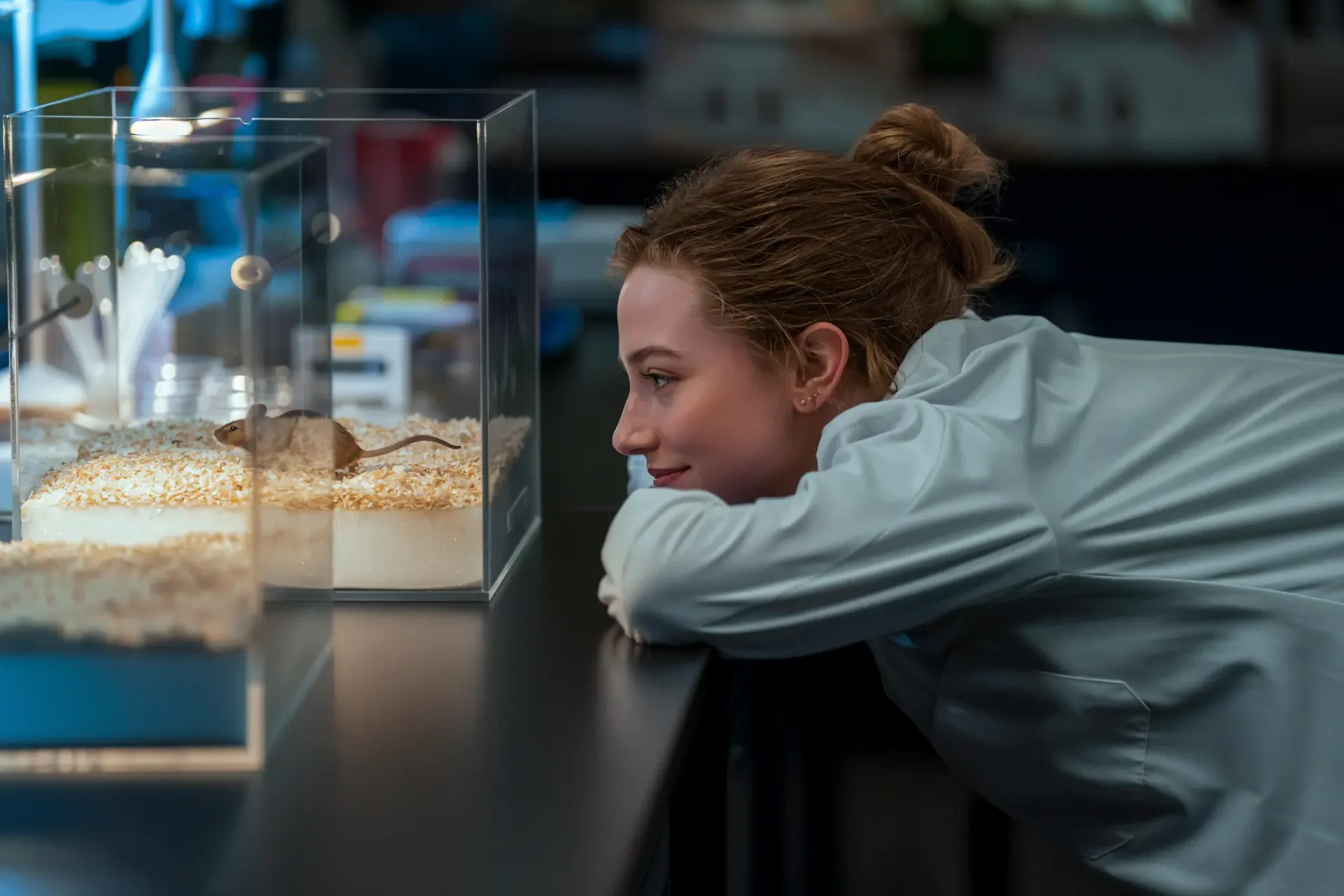 The Love Hypothesis scene: woman leans on a counter, smiling at small aquarium tanks — 4K Ultra HD PC desktop wallpaper/background.