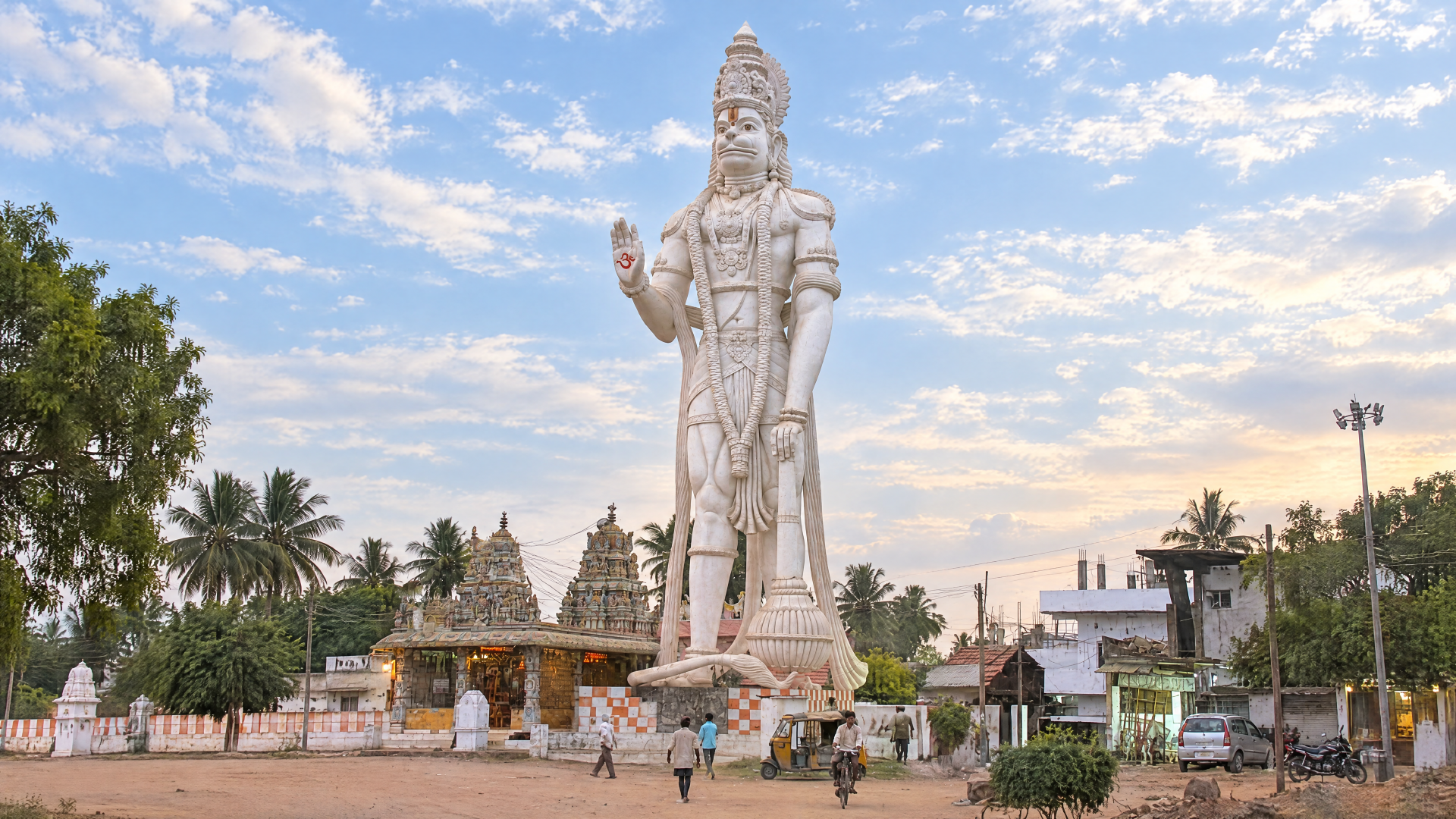Giant Lord Hanuman statue before a Hindu temple, ornate white sculpture and palm trees under a blue sky — 4K Ultra HD PC desktop wallpaper and background.