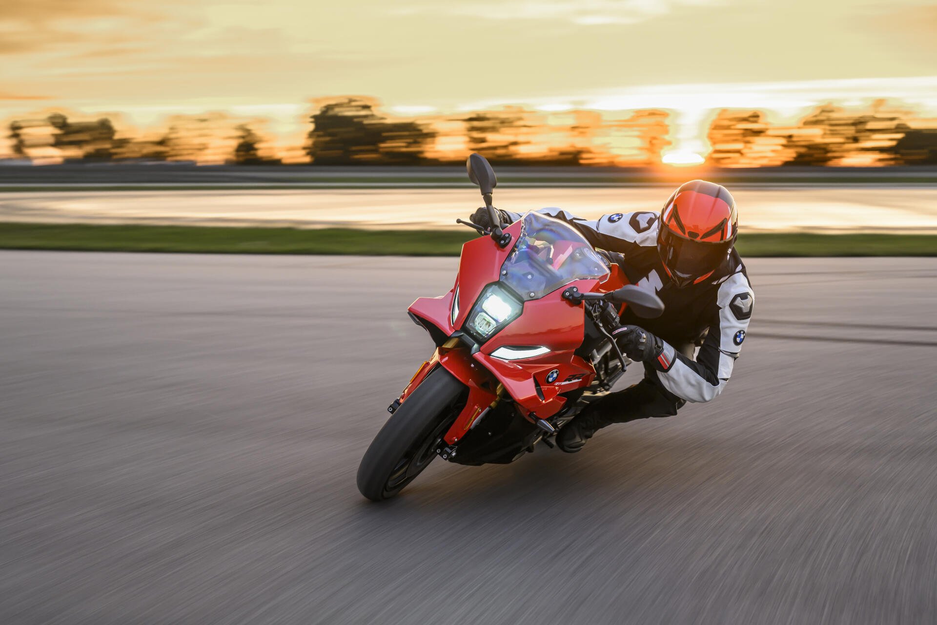 BMW F 450 RR motorcycle racer leaning through a track turn at sunset, 8K Ultra HD PC desktop wallpaper background.
