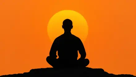 Zen silhouette of a person meditating on a rock before a large orange sun at sunset — 5K Ultra HD PC desktop wallpaper and background.