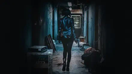 The Villainess — 4K Ultra HD PC wallpaper of a lone woman in a leather jacket walking down a dim, gritty corridor, pistol in hand toward a distant light.