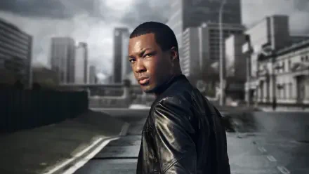 24: Legacy — 4K Ultra HD PC desktop wallpaper: a person in a leather jacket glances over their shoulder on a moody urban street with a towering skyline.