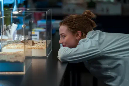 The Love Hypothesis scene: woman leans on a counter, smiling at small aquarium tanks — 4K Ultra HD PC desktop wallpaper/background.