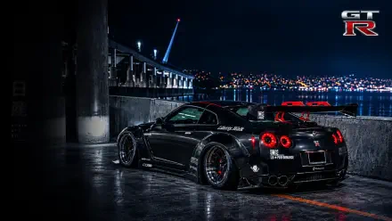 Black GTR-35 sports car by a waterfront at night, city lights reflecting on wet pavement — 2K Quad HD PC desktop wallpaper/background for computer.