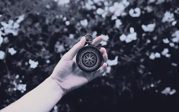 Digital art, digital painting, illustration: hand holding an antique compass against a blurred floral landscape — 5K Ultra HD PC desktop wallpaper and background artwork.
