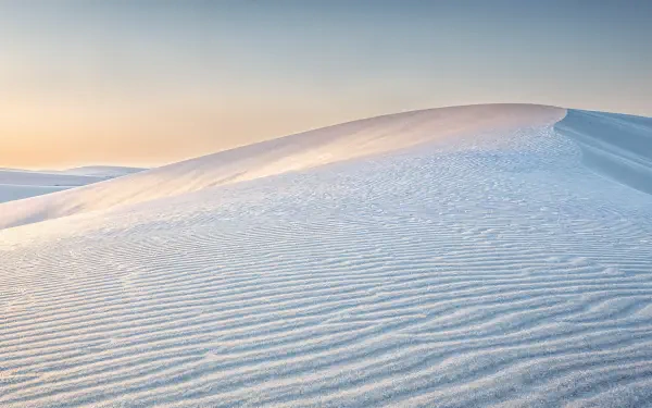 Minimal sand dune at sunrise with rippled, wind-sculpted textures and a soft pastel sky — 4K Ultra HD PC desktop wallpaper background.