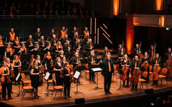 5K Ultra HD PC desktop wallpaper: full symphony orchestra onstage with conductor at center, musicians with strings, winds and brass under warm stage lighting.