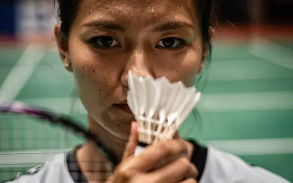Close-up of a badminton player holding a shuttlecock to her face with racket and court blurred behind — 4K Ultra HD PC desktop wallpaper and background.