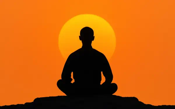 Zen silhouette of a person meditating on a rock before a large orange sun at sunset — 5K Ultra HD PC desktop wallpaper and background.