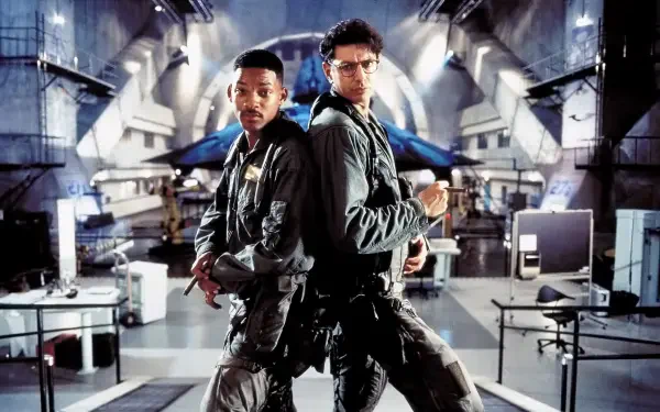 Independence Day 4K Ultra HD PC desktop wallpaper: two pilots in flight suits stand back-to-back in a giant military hangar, dramatic lighting and a glowing spacecraft in the background.