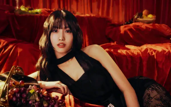 5K desktop wallpaper of a Japanese model with a k-pop idol–inspired look reclining on red velvet in a black dress, grapes arranged in the foreground.