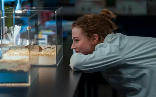 The Love Hypothesis scene: woman leans on a counter, smiling at small aquarium tanks — 4K Ultra HD PC desktop wallpaper/background.