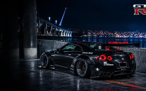 Black GTR-35 sports car by a waterfront at night, city lights reflecting on wet pavement — 2K Quad HD PC desktop wallpaper/background for computer.