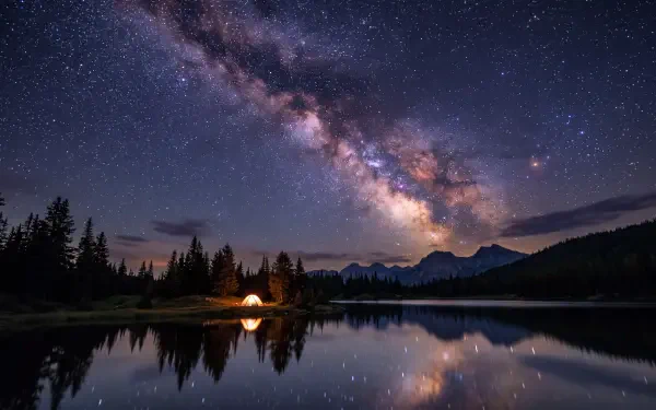 5K Ultra HD desktop wallpaper of the Milky Way and starry night sky reflected across a calm lake, framed by forest and distant mountains.