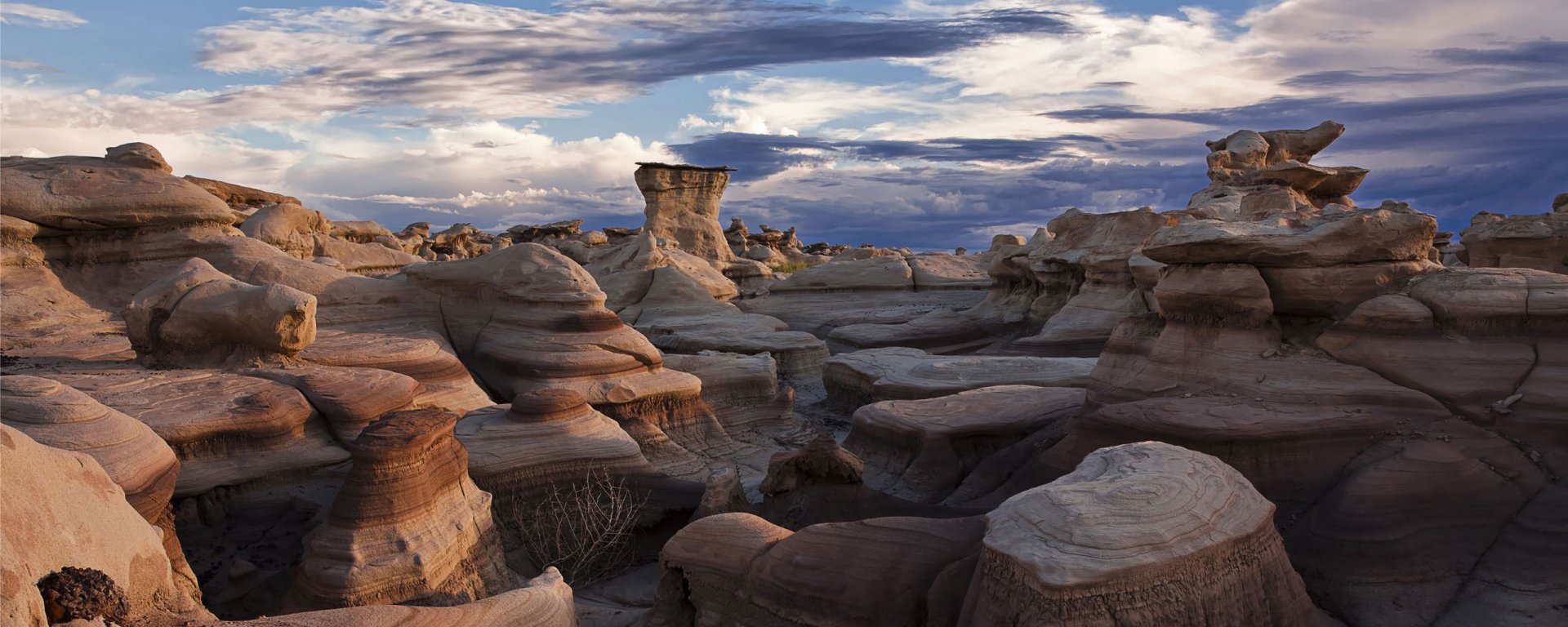 Weird Bisti landscape in New Mexico: sculpted rock hoodoos and eroded formations under dramatic clouds, HD PC desktop wallpaper background.