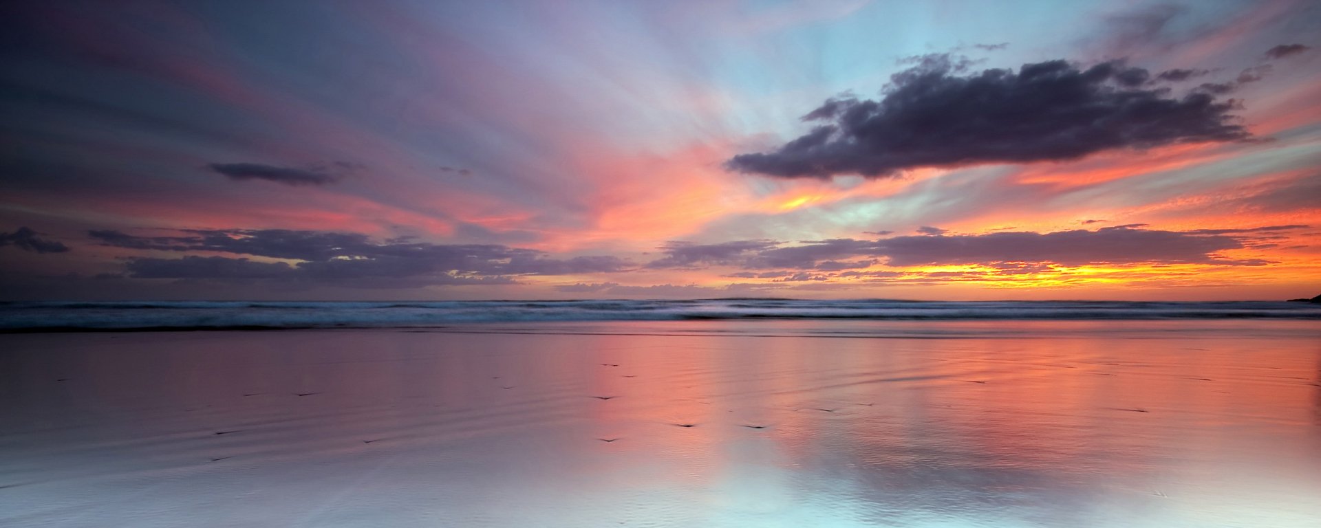 HD PC desktop wallpaper of a serene beach at sunset with soft pastel skies and gentle waves reflecting vibrant colors over the calm water.
