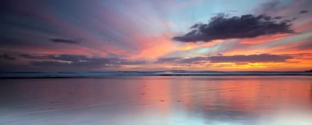 HD PC desktop wallpaper of a serene beach at sunset with soft pastel skies and gentle waves reflecting vibrant colors over the calm water.
