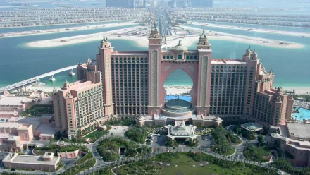 Aerial view of a luxurious man-made resort in Dubai, featuring grand architecture with a central arch, surrounded by water and greenery. HD desktop wallpaper and background.