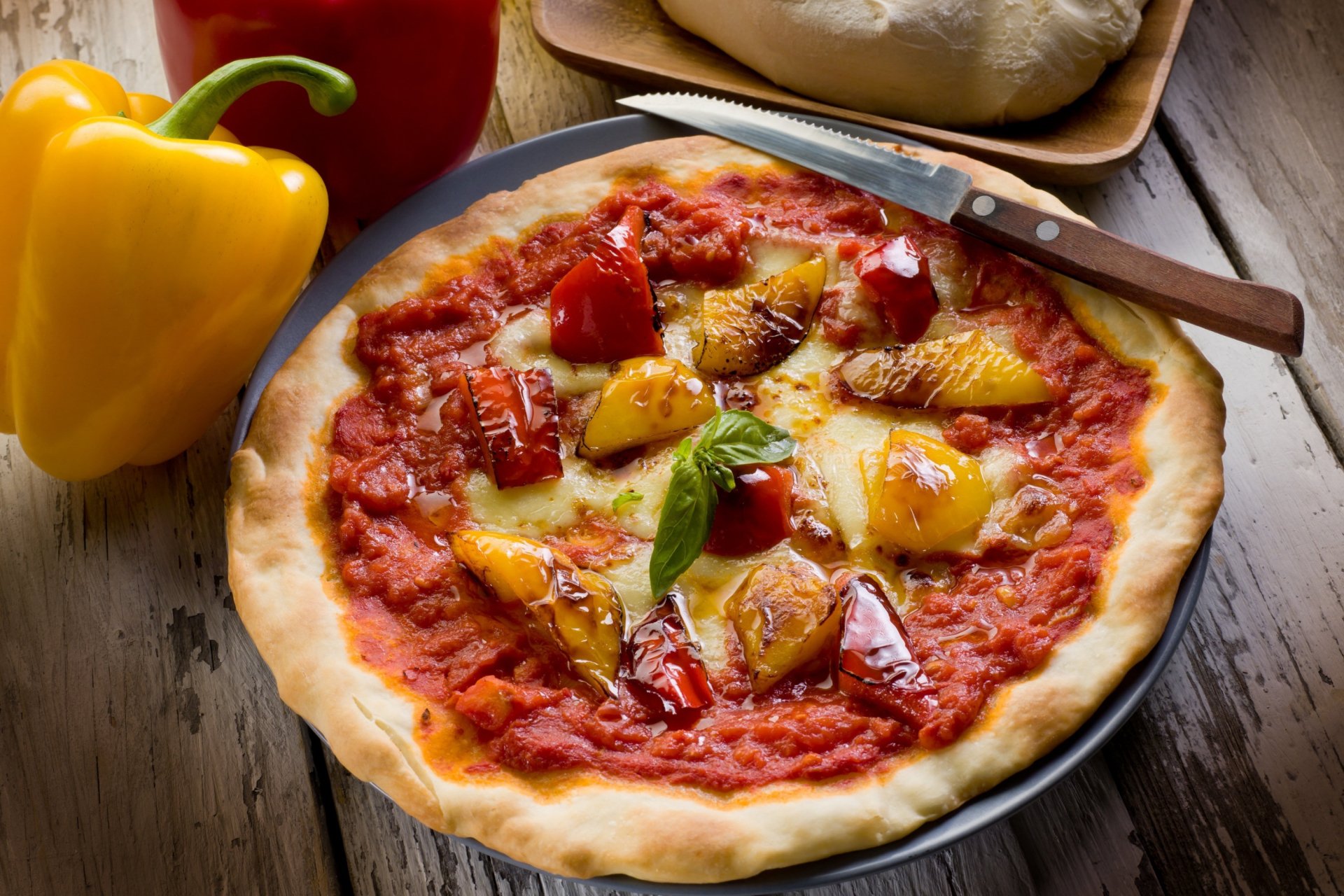 A delicious pizza topped with peppers and basil, set on a rustic wooden surface, accompanied by fresh ingredients, creating an inviting HD desktop wallpaper and background.