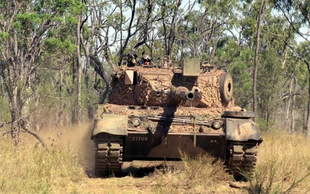 HD desktop wallpaper showing a military tank moving through dense bushland, with soldiers and a gun mounted on the tank during a war scenario.