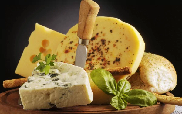 Food: cheese assortment on a wooden board — wedges, herb-crusted rounds, blue cheese, basil and crackers; 5K Ultra HD PC desktop wallpaper/background.