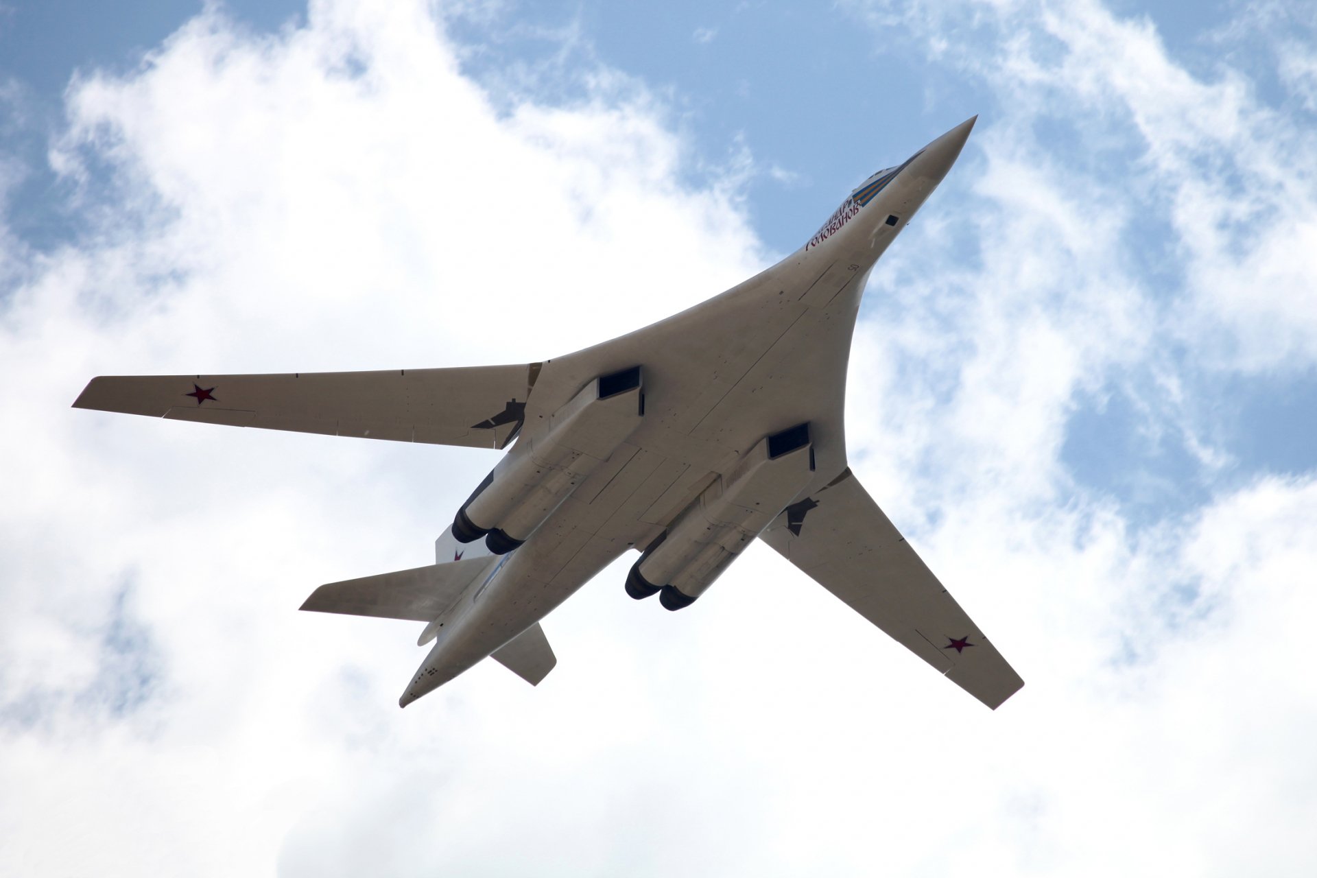A Tupolev Tu-160 military bomber soars through a cloud-dotted sky, showcasing its impressive wingspan and sleek design in this high-definition desktop wallpaper.