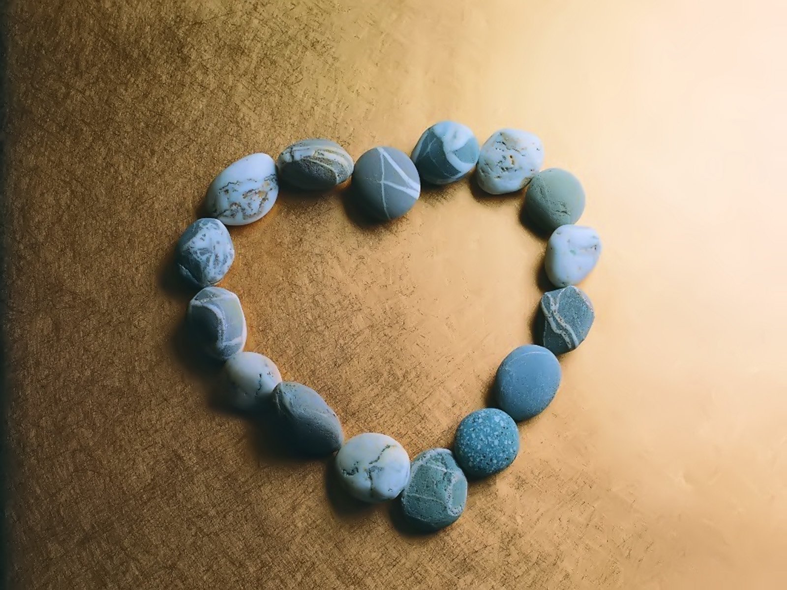 A heart-shaped arrangement of blue stones rests on a golden background, capturing an artistic expression of love. This HD wallpaper enhances any desktop with its serene design.