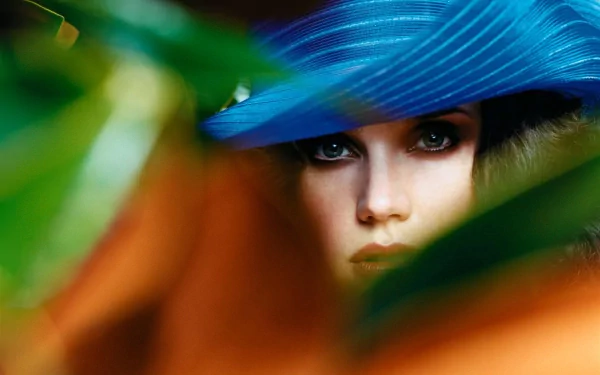 HD desktop wallpaper featuring a close-up of celebrity Jennifer Connelly wearing a striking blue hat, partially obscured by blurred foreground elements.