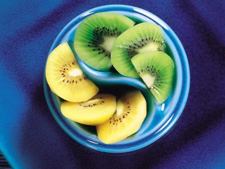 HD desktop wallpaper featuring a close-up of sliced green and yellow kiwi arranged in a yin-yang pattern on a blue plate against a deep blue background.