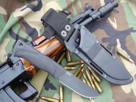 HD desktop wallpaper featuring a man-made assault rifle with a tactical knife and scattered bullets on a camouflage fabric background.