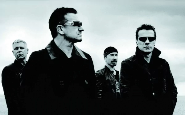 HD PC desktop wallpaper: monochrome portrait of a four-member rock band in sunglasses and dark coats standing against an overcast sky, music-themed background.