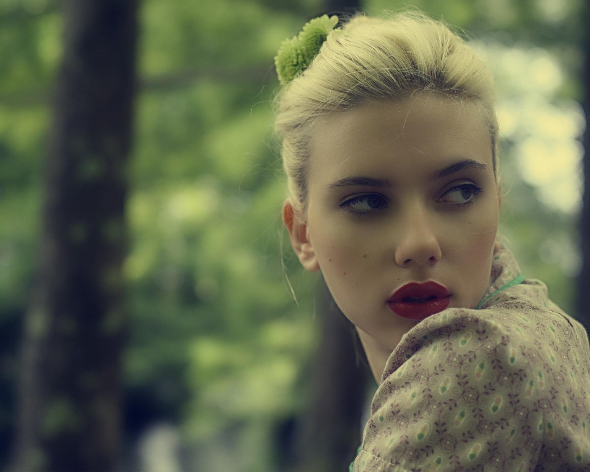 HD desktop wallpaper featuring Scarlett Johansson in an outdoor setting, looking to her right with a serene background of blurred greenery and trees.