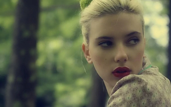 HD desktop wallpaper featuring Scarlett Johansson in an outdoor setting, looking to her right with a serene background of blurred greenery and trees.